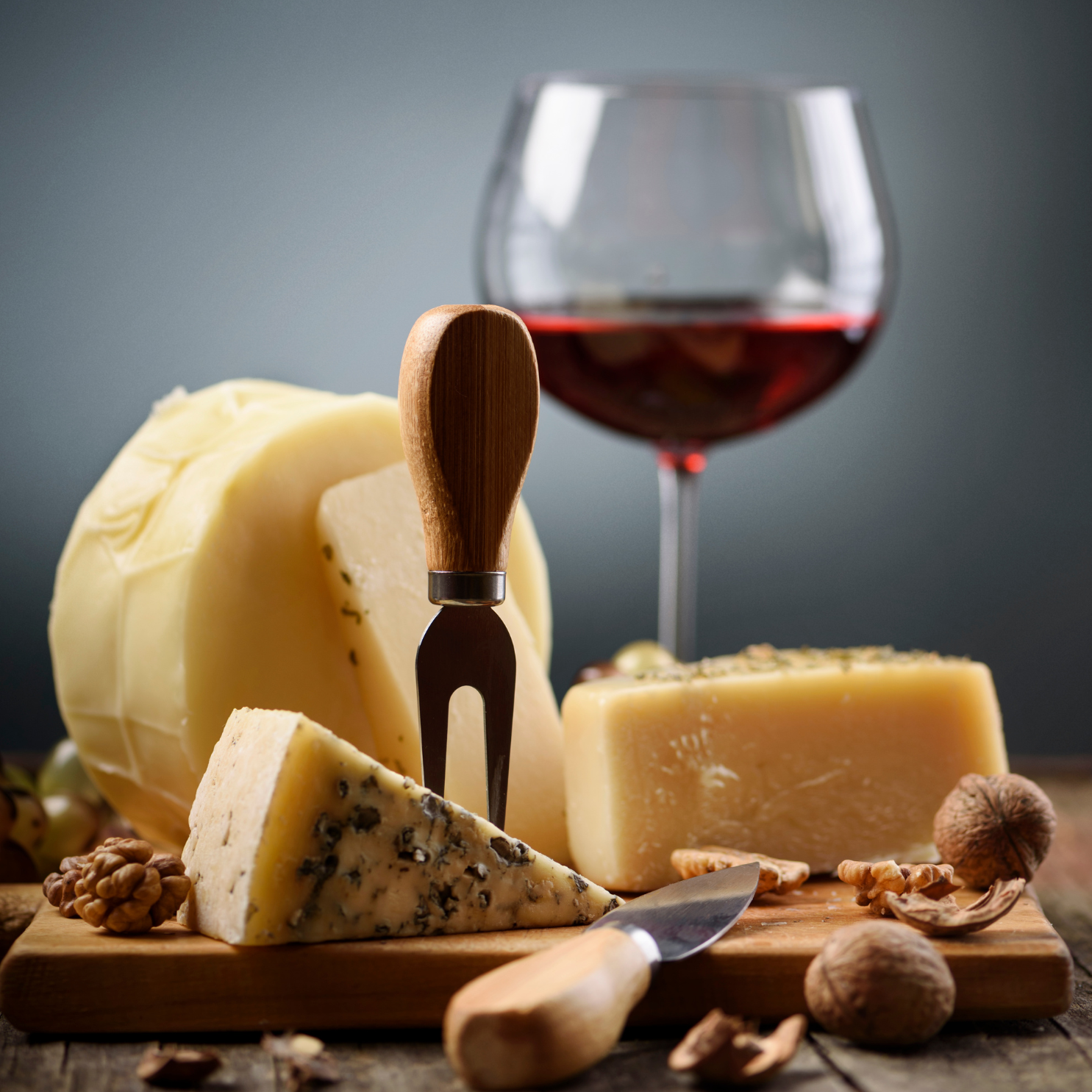 A wooden board of cheeses and walnuts beside a glass of red wine.