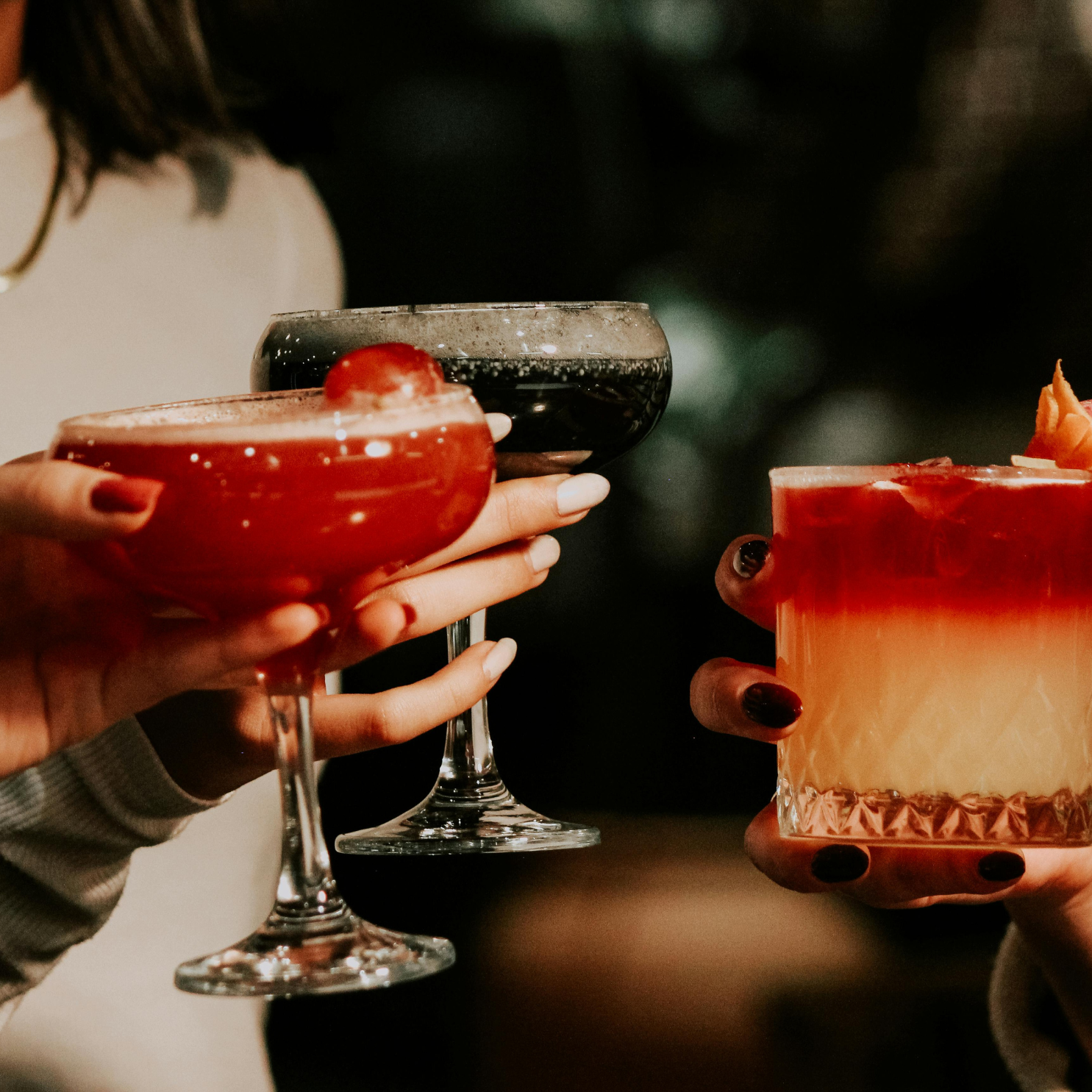 Three cocktails held together for a toast in warm evening light.